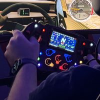 Hands on a lit racing wheel, its LED display and buttons glowing